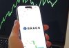 Un celular con el logo de Bragg Gaming frente a un gráfico financiero ascendente.