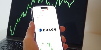 Un celular con el logo de Bragg Gaming frente a un gráfico financiero ascendente.