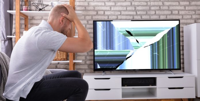 Un hombre se toma la cabeza frente a un televisor roto.