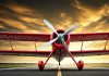 Un avión biplano rojo detenido sobre una pista de aterrizaje.