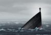 Un hombre de pie sobre la proa de un barco que se hunde en el mar.