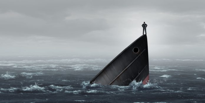 Un hombre de pie sobre la proa de un barco que se hunde en el mar.