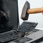 Una persona destruye una computadora portátil con un martillo.