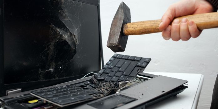 Una persona destruye una computadora portátil con un martillo.