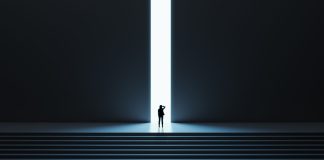 Una mujer avanza sobre una puerta iluminada en la cima de unas escaleras.