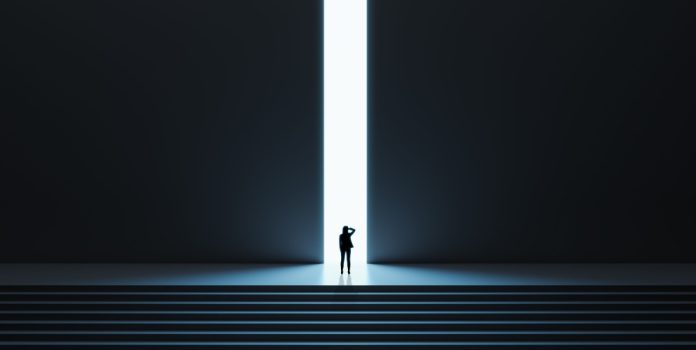 Una mujer avanza sobre una puerta iluminada en la cima de unas escaleras.
