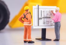 Gente en miniatura observa planos de construcción.