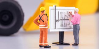 Gente en miniatura observa planos de construcción.