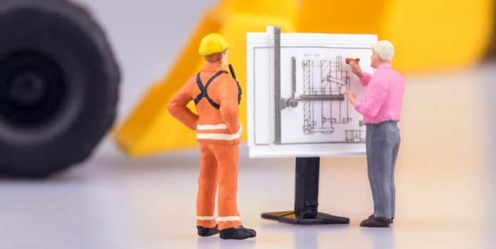 Gente en miniatura observa planos de construcción.