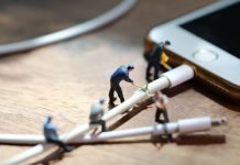 Hombres en miniatura cortan un cable conectado a un celular.