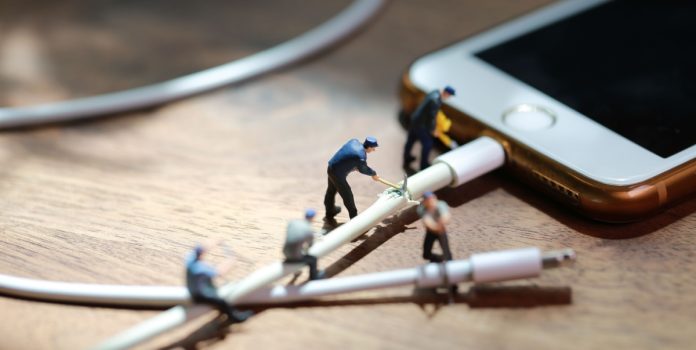 Hombres en miniatura cortan un cable conectado a un celular.